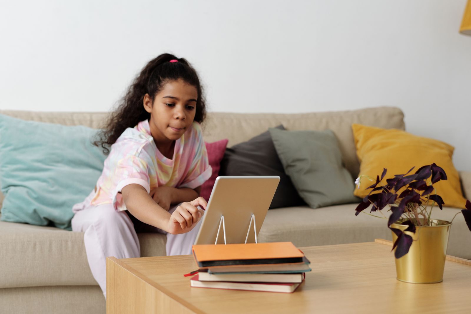 A girl on a sofa tapping the screen of a tablet standing on a coffee table