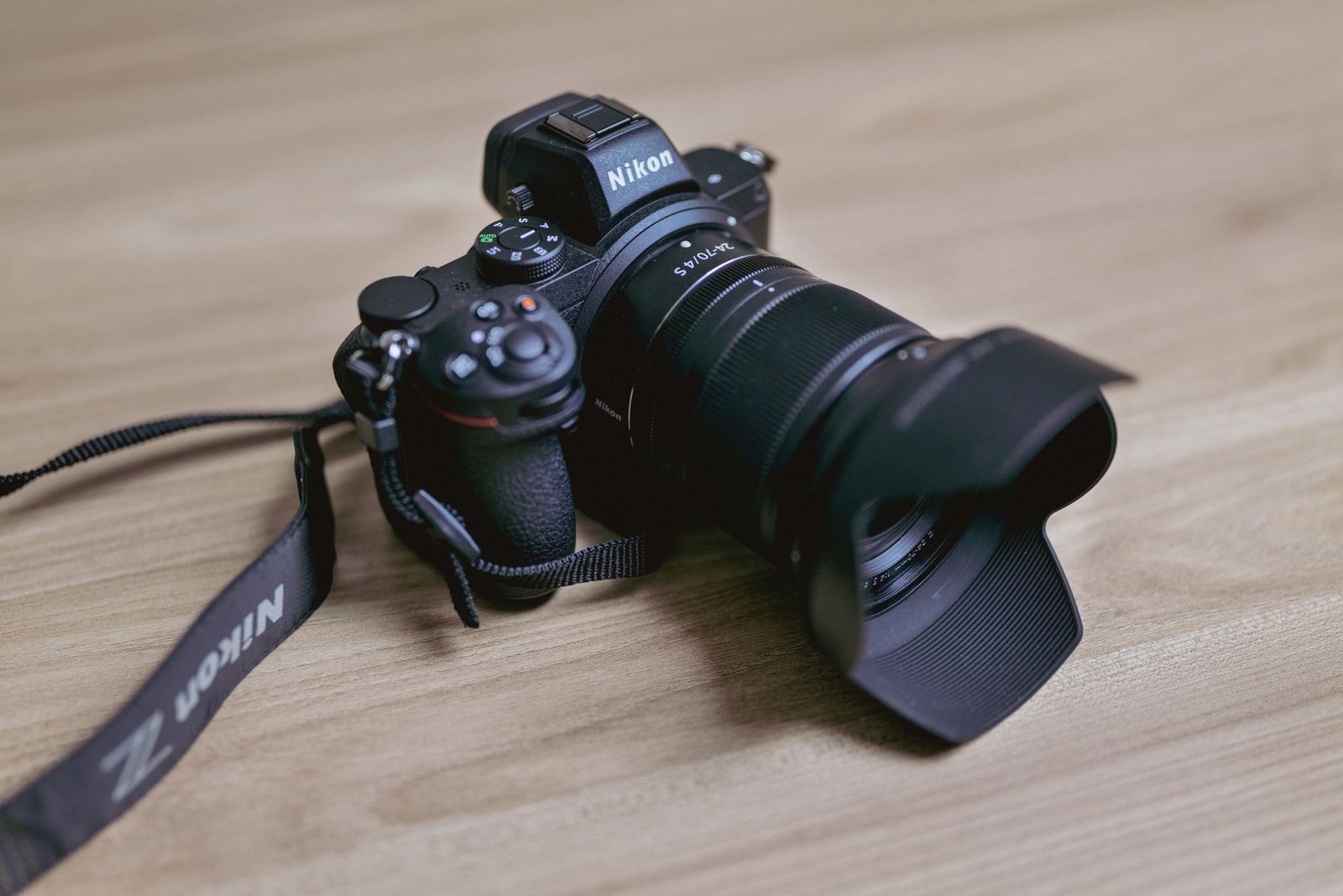 Black mirrorless camera with a zoom lens and neck strap resting on a light wooden table