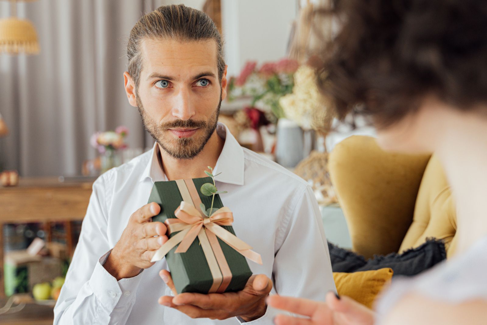 A man in a white shirt holding a wrapped gift box tied with a ribbon