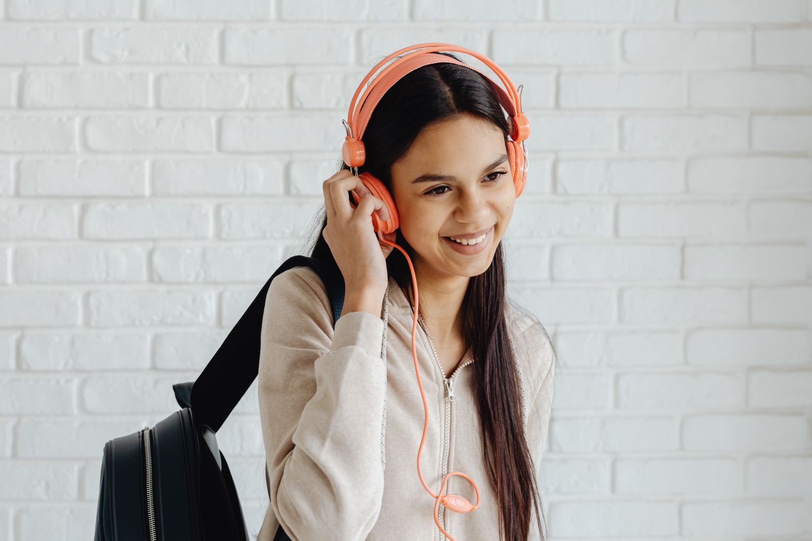 A smiling teenager wearing pink headphones and holding a backpack indoors